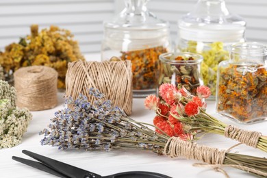 Bunches of dry flowers, different medicinal herbs and spools on white wooden table