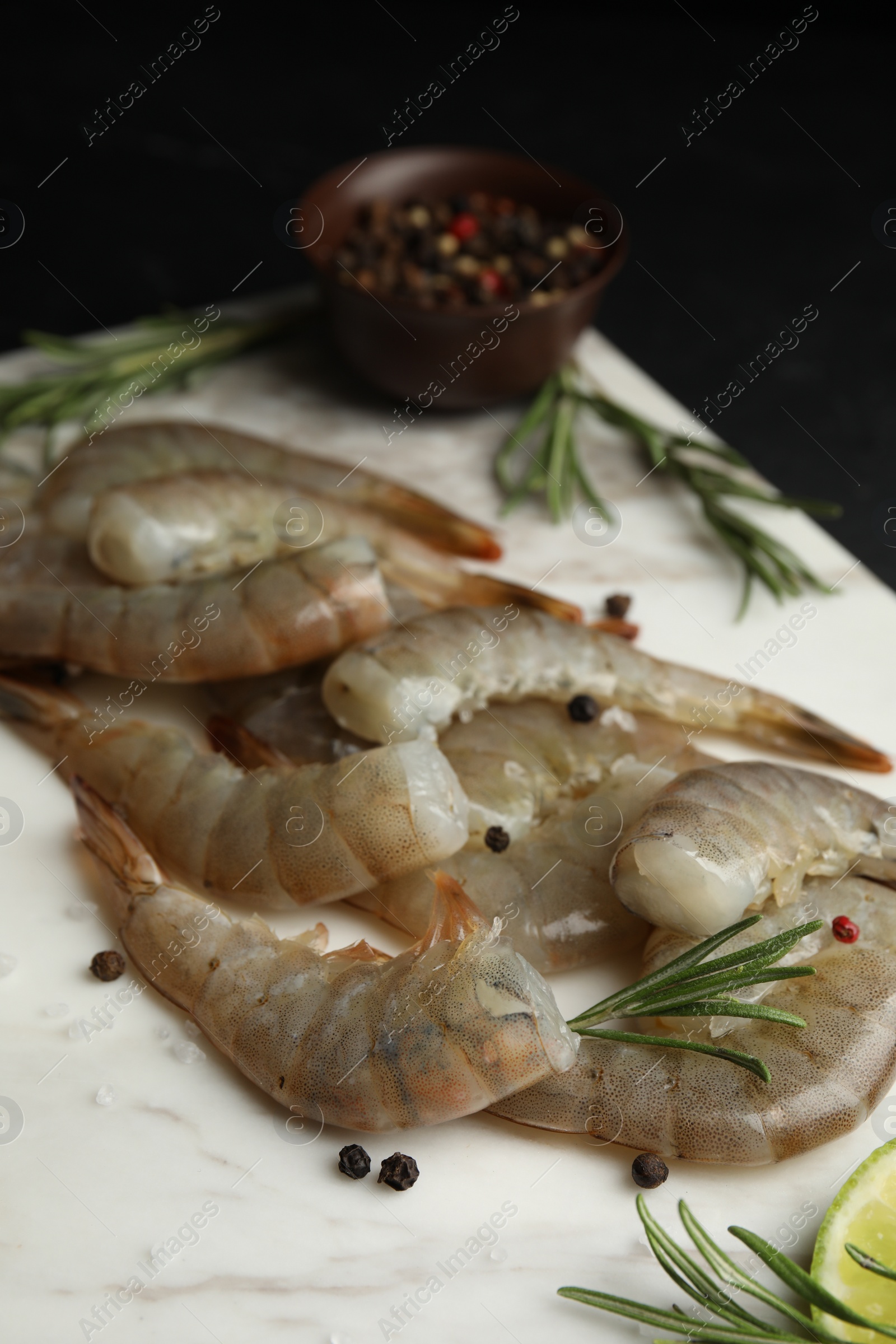 Photo of Fresh raw shrimps with rosemary and pepper on marble board, closeup