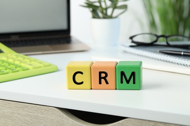 Photo of Abbreviation CRM of cubes with laptop on white office table. Customer Relationship Management