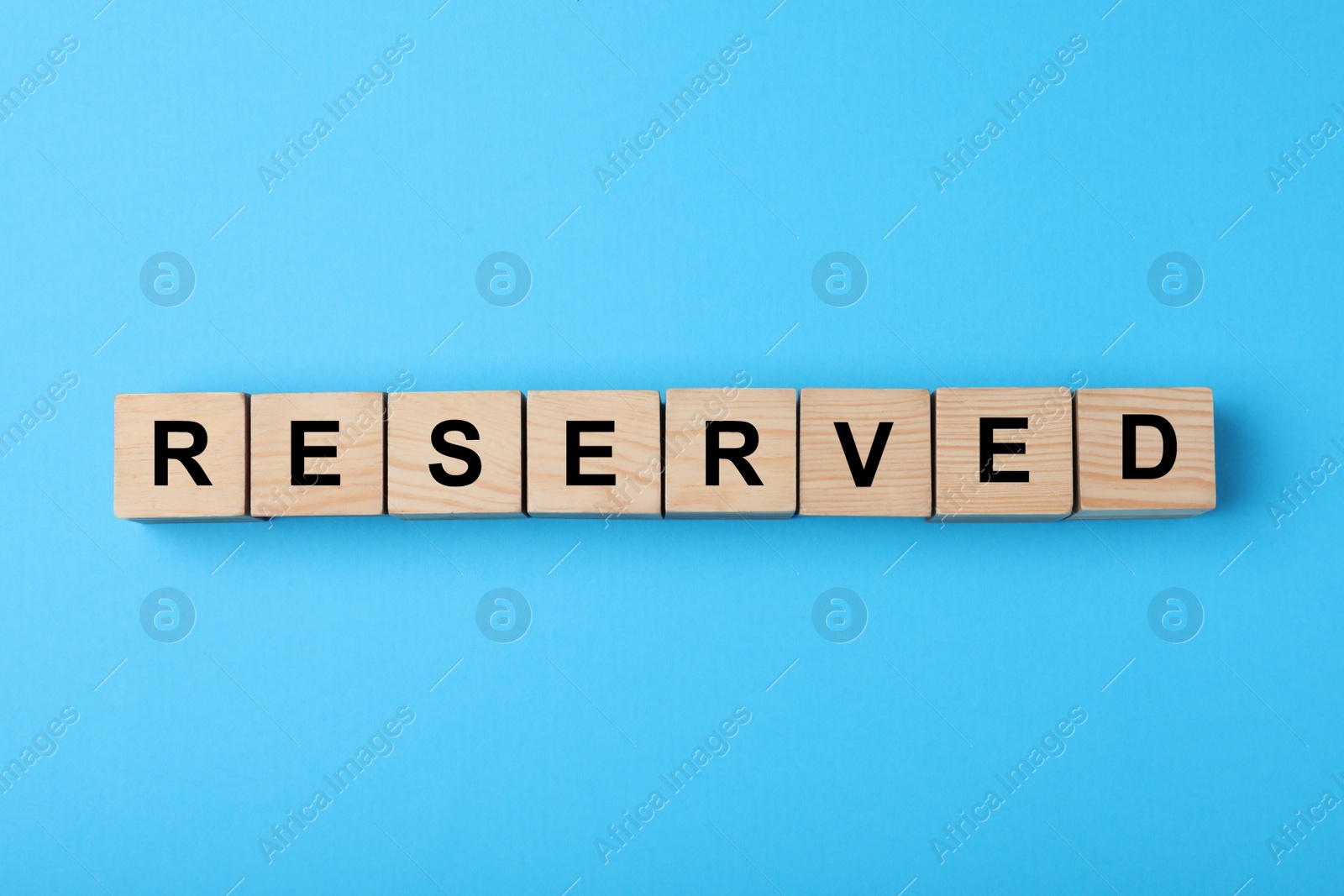 Photo of Wooden cubes with word Reserved on light blue background, flat lay