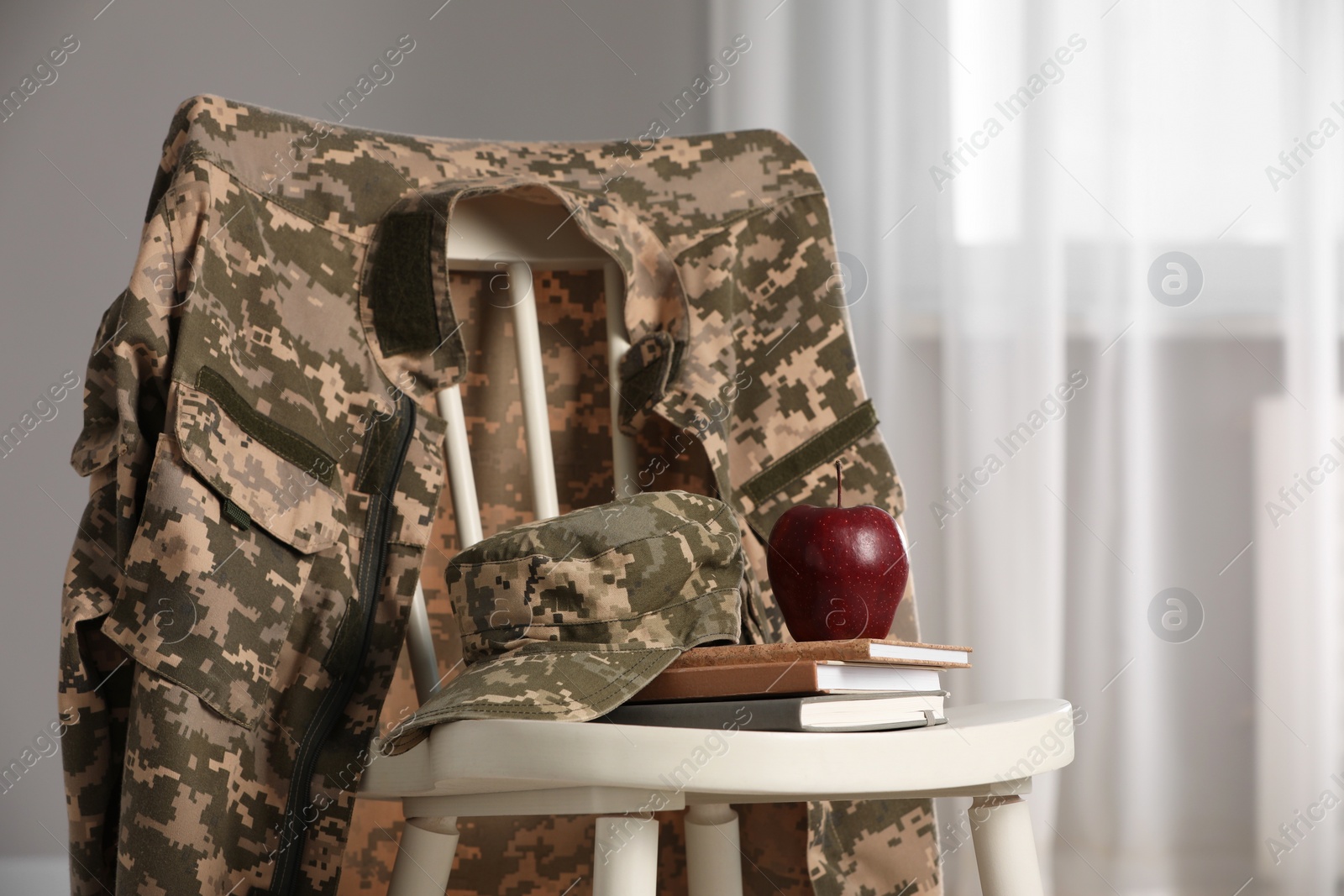 Photo of Chair with soldier uniform, notebooks and apple indoors. Military education