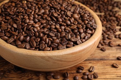 Photo of Bowl of roasted coffee beans on wooden table, closeup