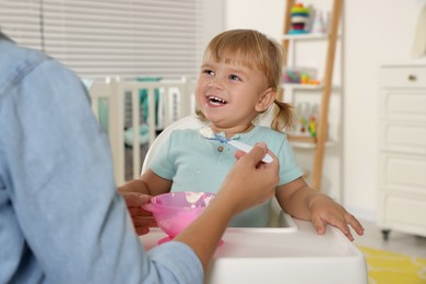 Mother feeding her cute little child with yogurt at home