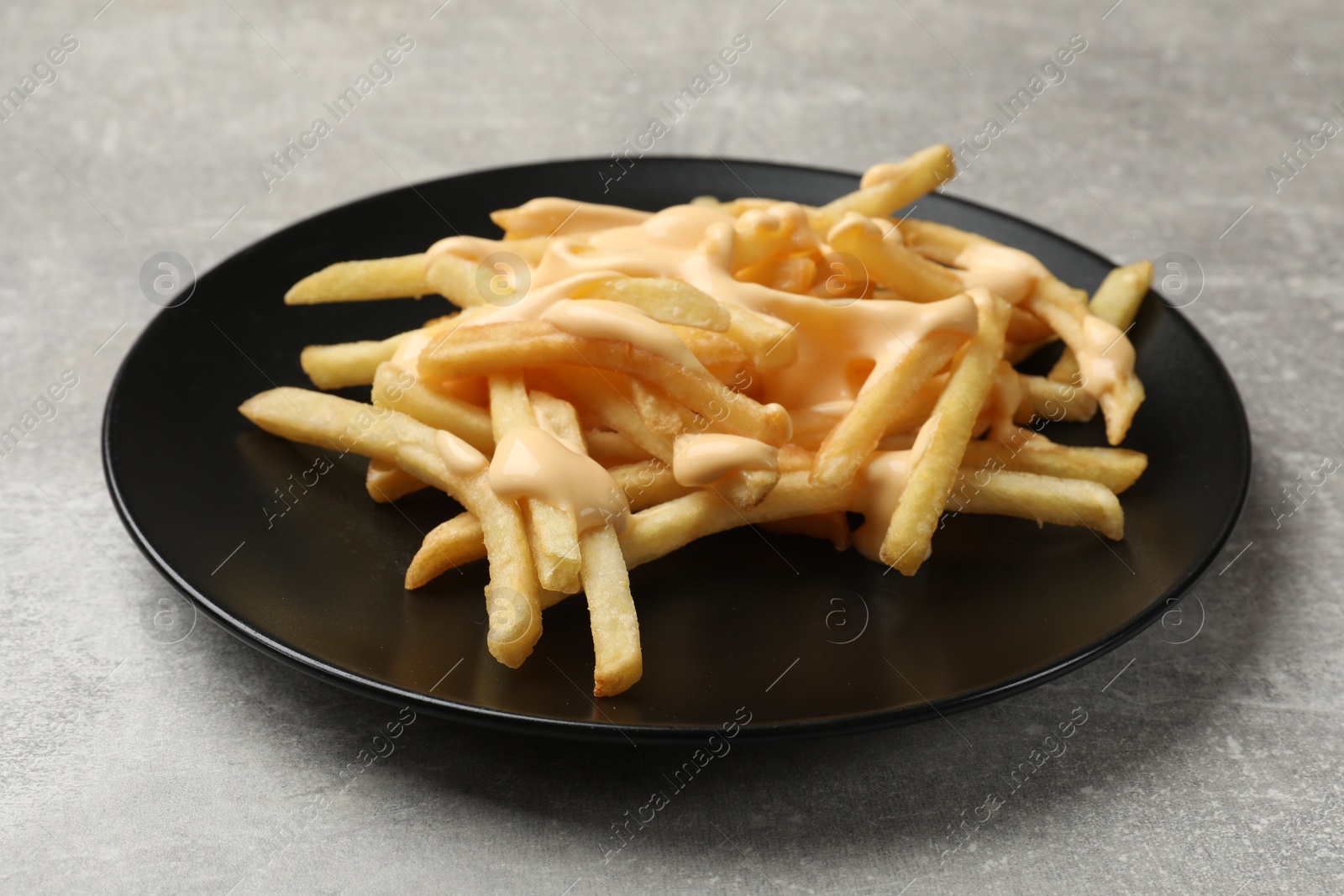 Photo of Delicious French fries with cheese sauce on grey table, closeup