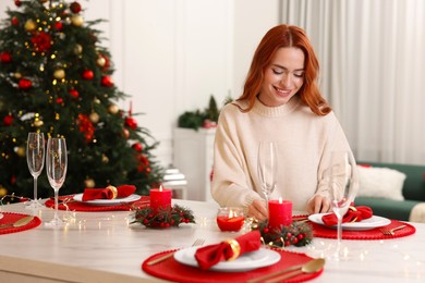 Beautiful young woman setting table in room decorated for Christmas