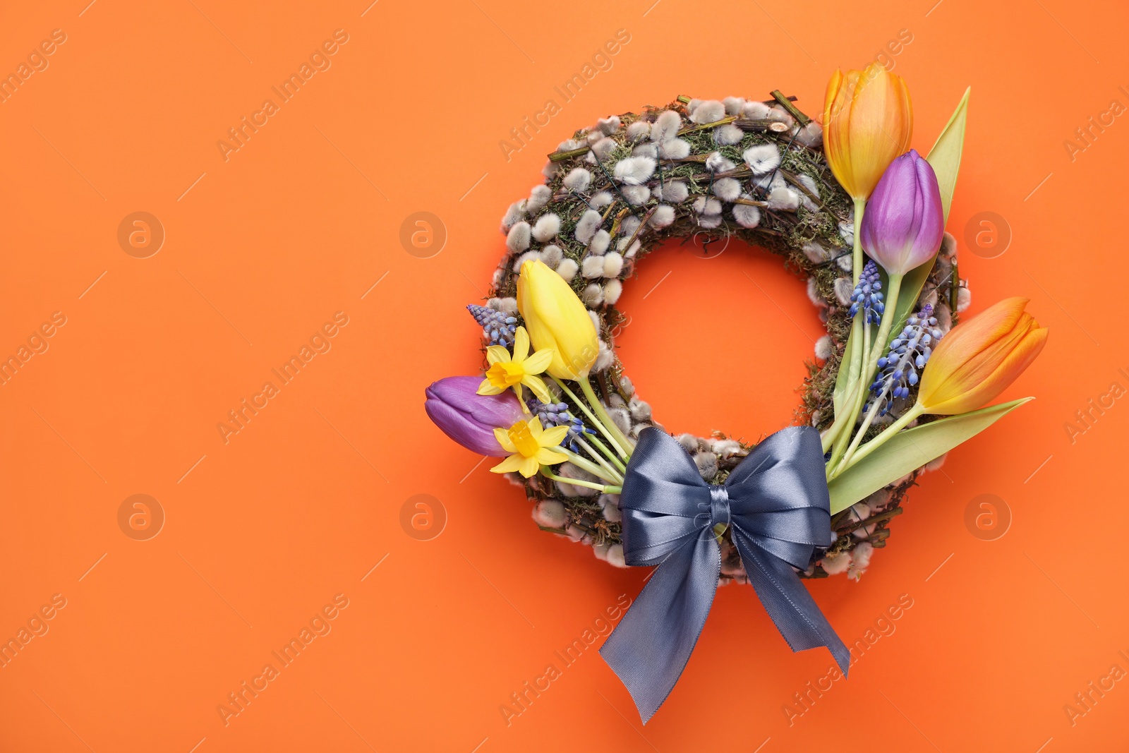 Photo of Willow wreath with different beautiful flowers and grey bow on orange background, top view. Space for text