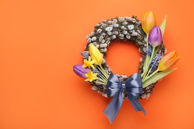Photo of Willow wreath with different beautiful flowers and grey bow on orange background, top view. Space for text