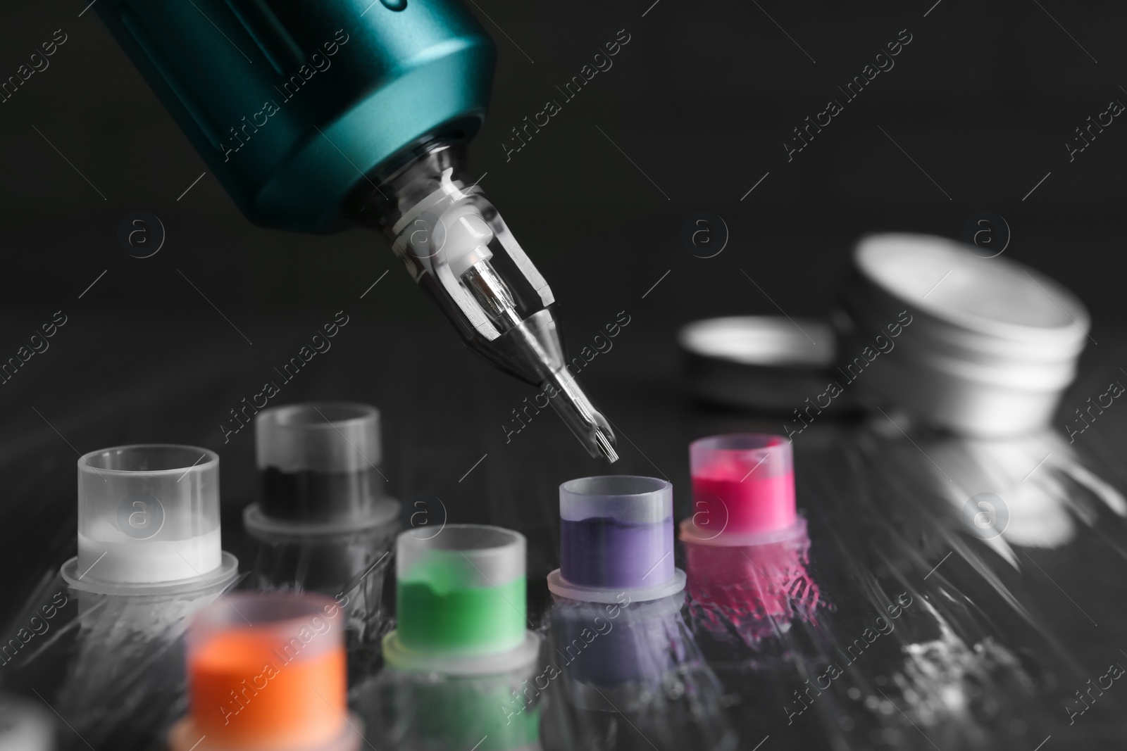 Photo of Modern professional tattoo machine and caps with colorful inks on table, closeup