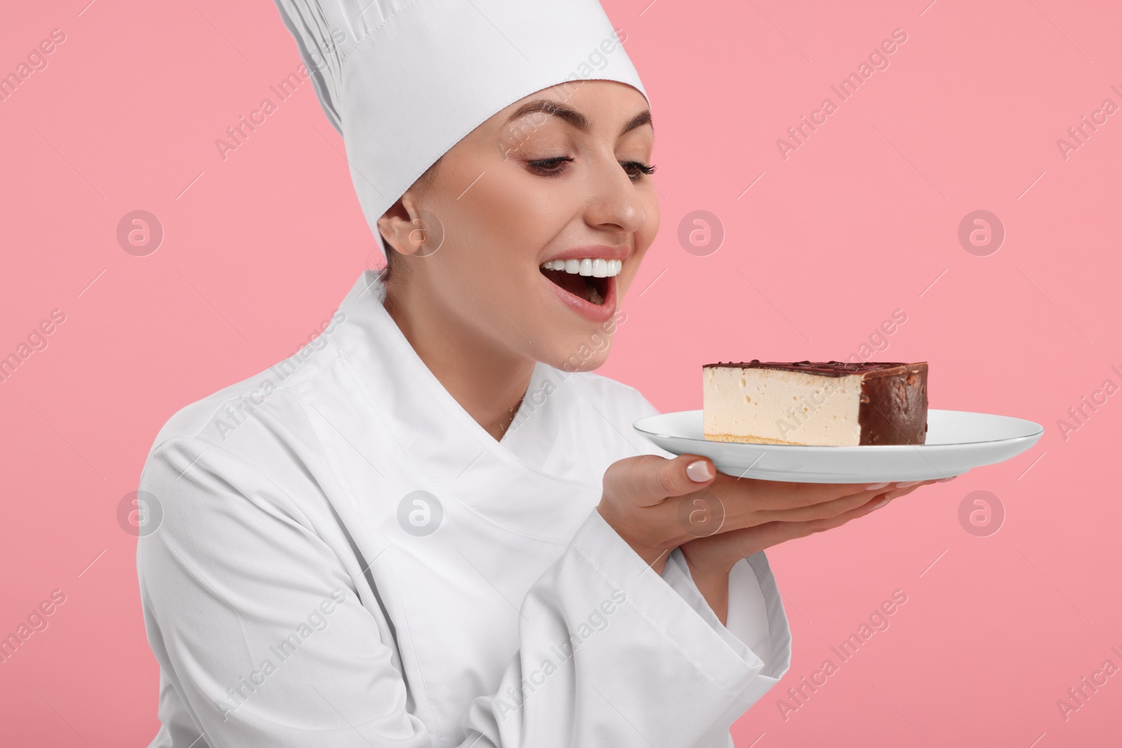 Photo of Happy professional confectioner in uniform holding delicious cheesecake on pink background