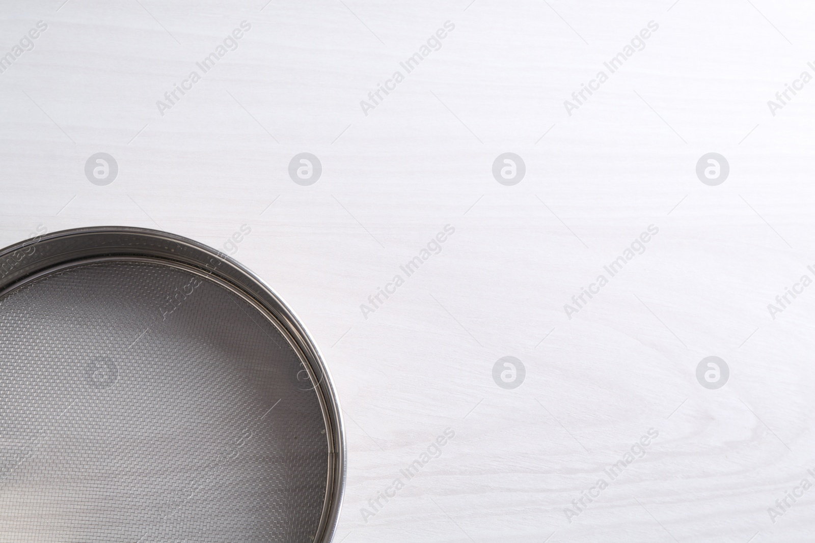 Photo of One metal sieve on white wooden table, top view. Space for text