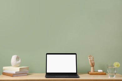 Photo of Stylish workplace with laptop, books and decor on table near light green wall