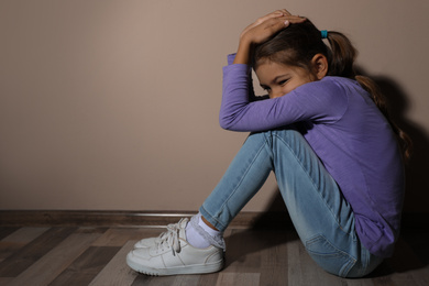 Photo of Scared little girl near beige wall, space for text. Domestic violence concept