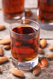 Photo of Shot glass with tasty amaretto liqueur and almonds on wooden table, closeup