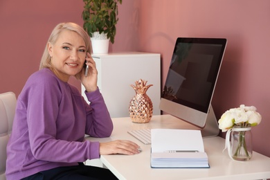 Photo of Mature woman talking on mobile phone at workplace