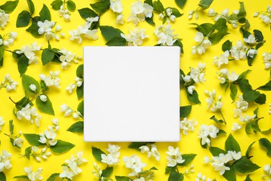 Photo of Blank canvas and beautiful jasmine flowers on yellow background, flat lay. Space for design
