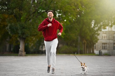 Photo of Man running with adorable Jack Russell Terrier on city street. Dog walking
