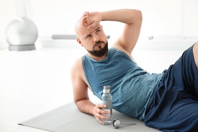 Tired overweight man with bottle of water in gym