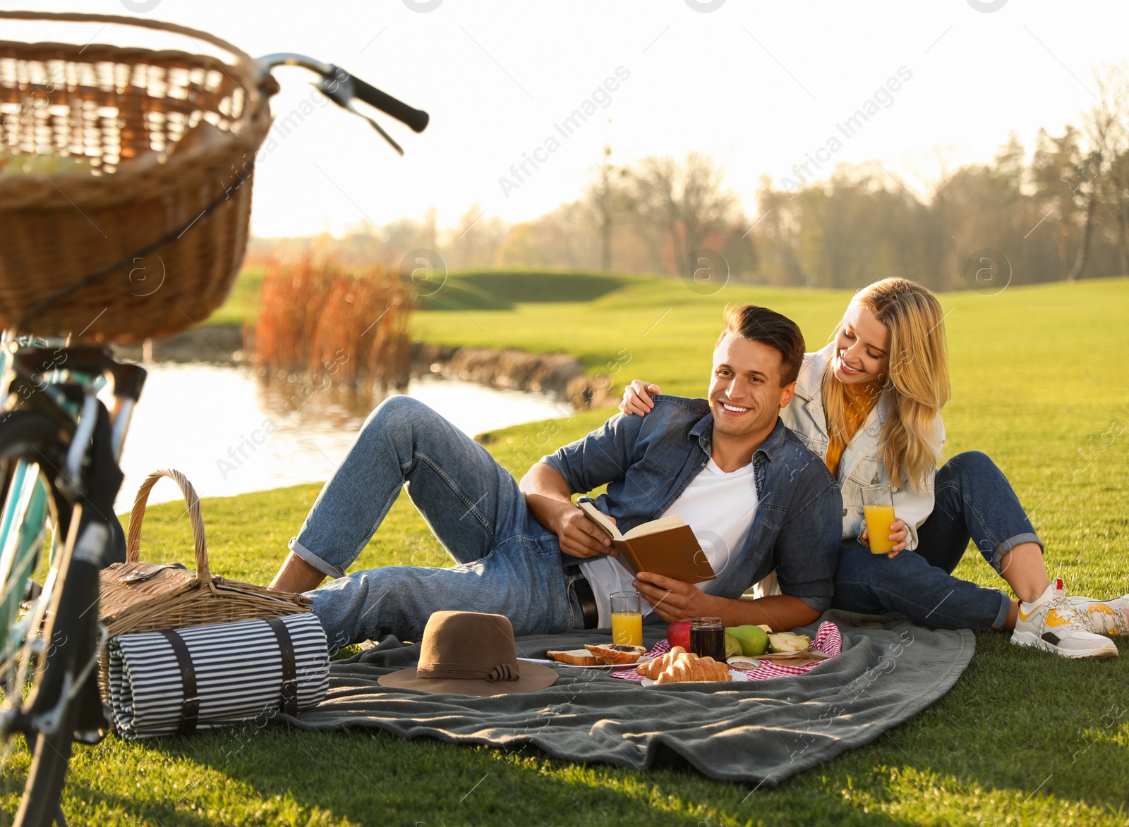 Photo of Happy young couple having picnic near lake on sunny day