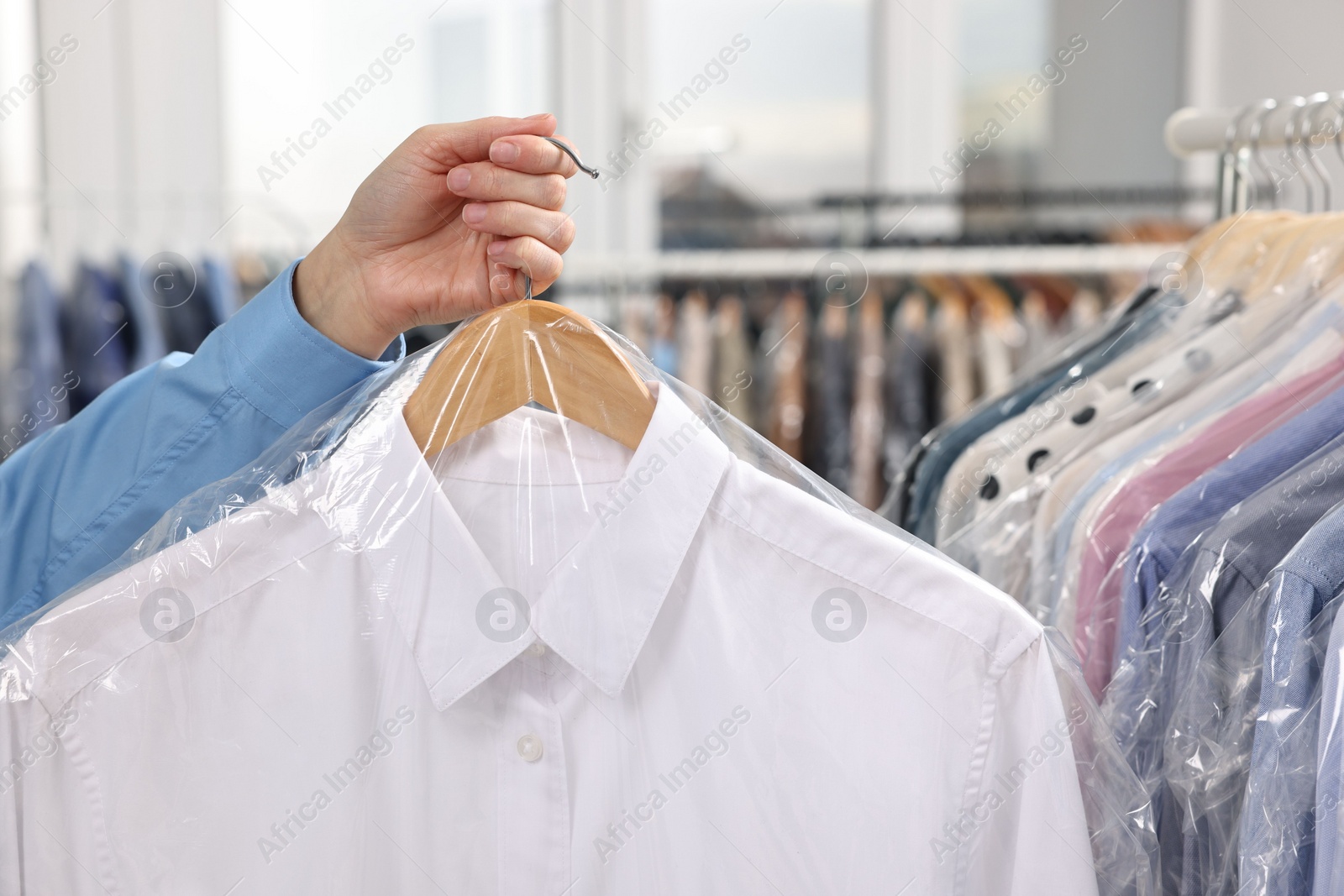 Photo of Dry-cleaning service. Woman holding shirt in plastic bag indoors, closeup