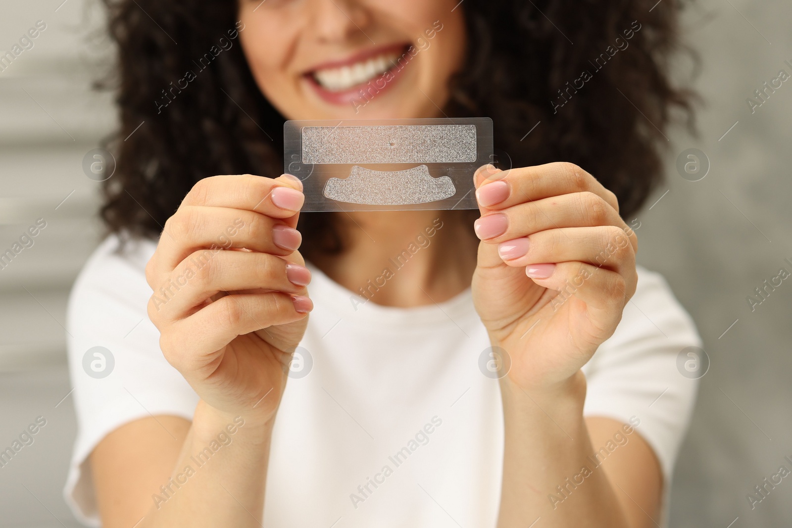 Photo of Young woman holding teeth whitening strips on blurred background, closeup