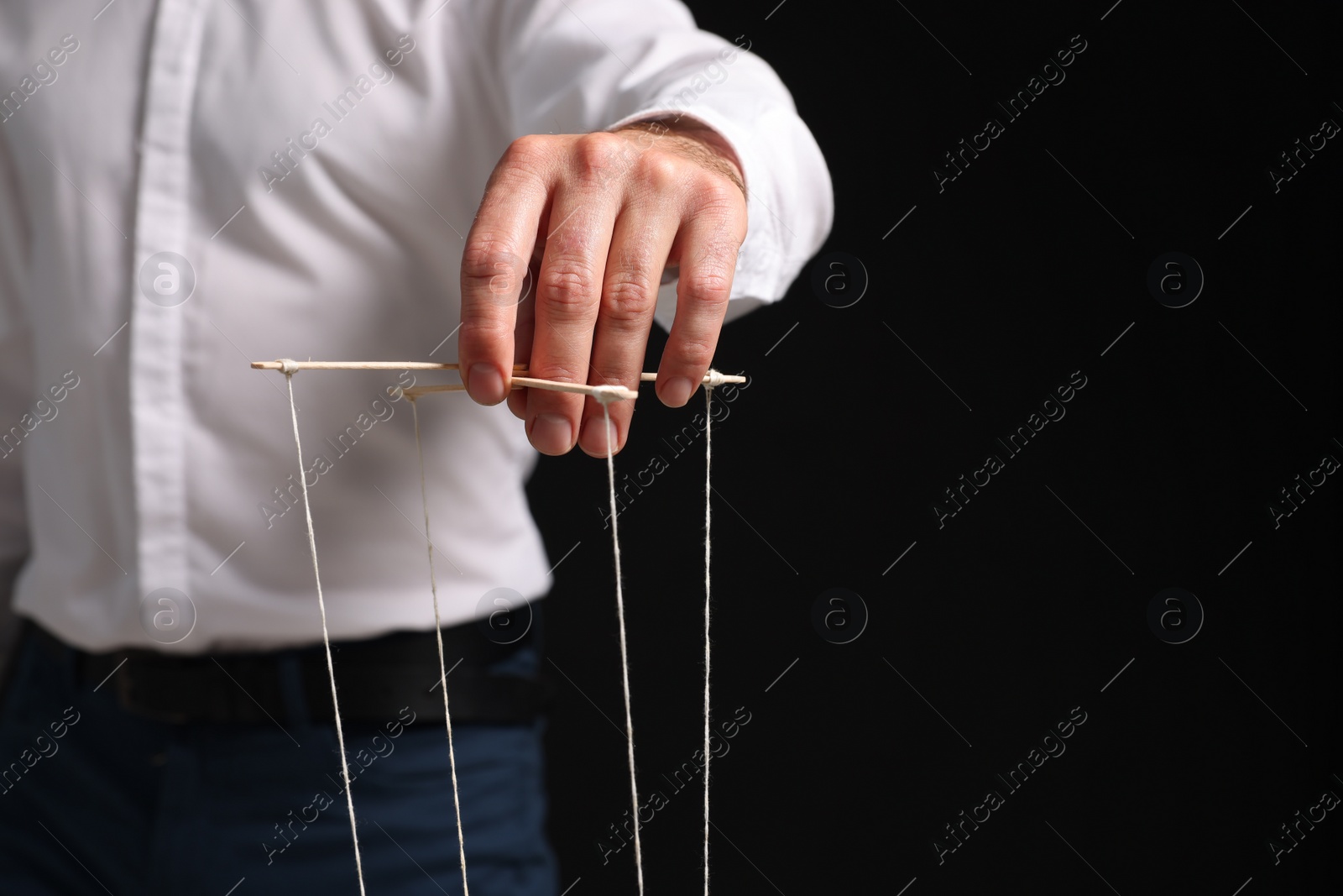 Photo of Man in formal outfit pulling strings of puppet on black background, closeup. Space for text