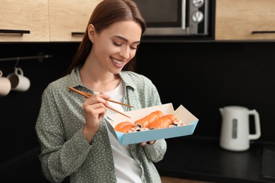 Beautiful young woman eating sushi rolls with chopsticks in kitchen