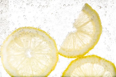 Photo of Juicy lemon slices in soda water against white background, closeup