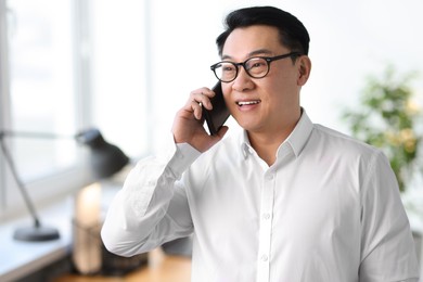 Photo of Portrait of smiling businessman talking by smartphone in office