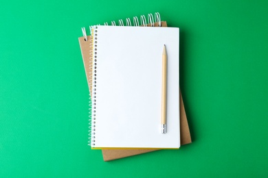 Photo of Notebooks with pencil on green background, top view