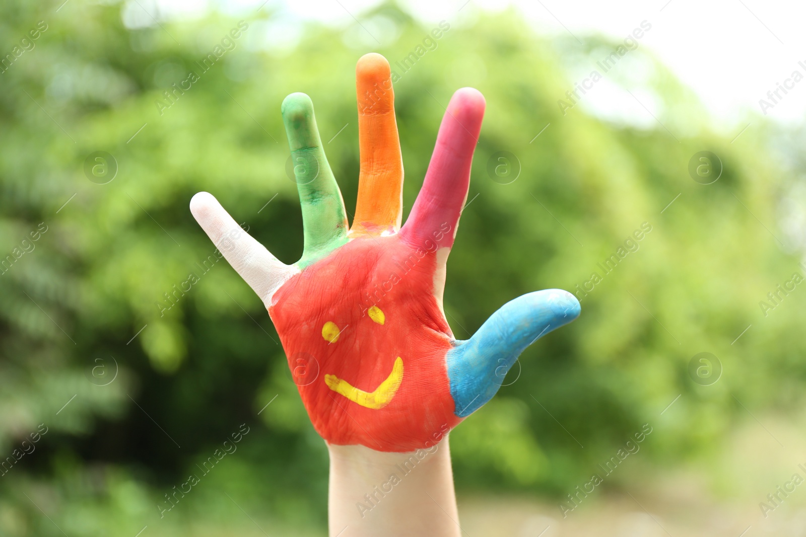 Photo of Kid with smiling face drawn on palm in green park, closeup