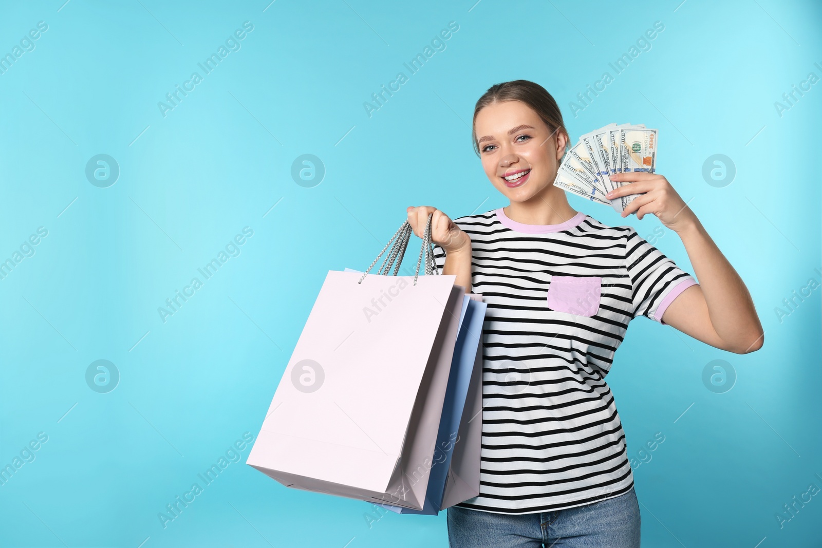 Photo of Portrait of happy young woman with money and shopping bags on color background. Space for text