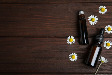 Bottles of essential oil and chamomiles on wooden table, flat lay. Space for text