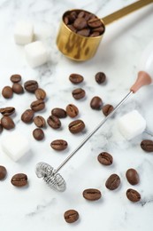 Milk frother wand, sugar cubes and coffee beans on white marble table, above view