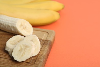 Photo of Cut and whole bananas on coral background, closeup. Space for text