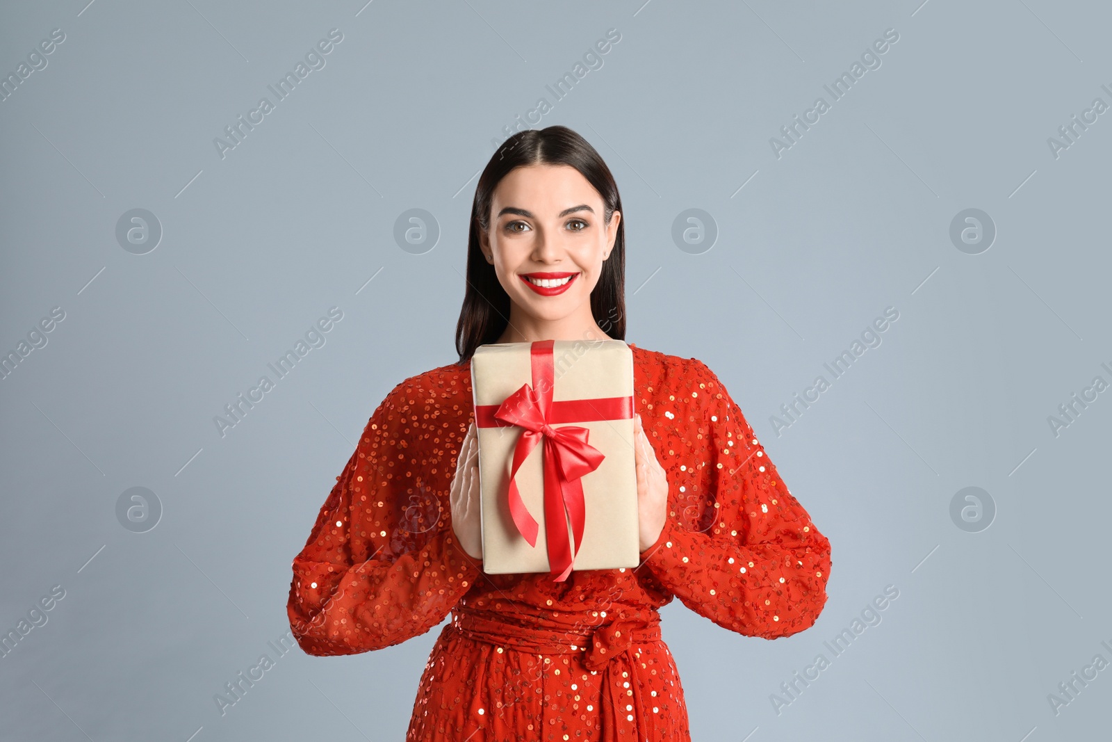 Photo of Woman in red dress holding Christmas gift on grey background