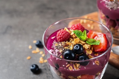 Photo of Delicious acai dessert with granola and berries served on grey table, closeup. Space for text