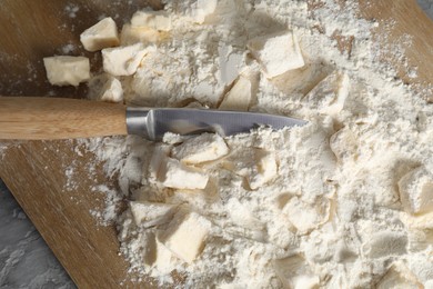 Photo of Making shortcrust pastry. Flour, butter, knife and wooden board on grey table, top view