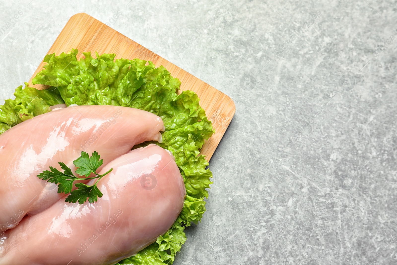 Photo of Wooden board with raw chicken breasts and lettuce on grey background, top view. Space for text