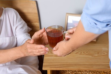 Photo of Caregiver giving tea to elderly woman at home, closeup
