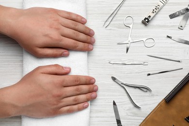 Photo of Man holding hands on towel near set of manicure tools at white wooden table, top view