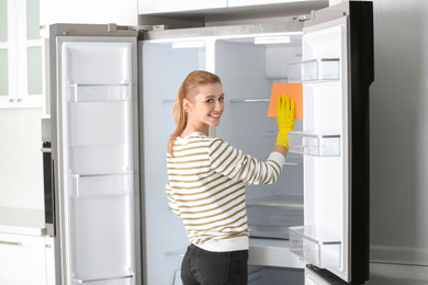 Photo of Woman in rubber gloves cleaning empty refrigerator at home