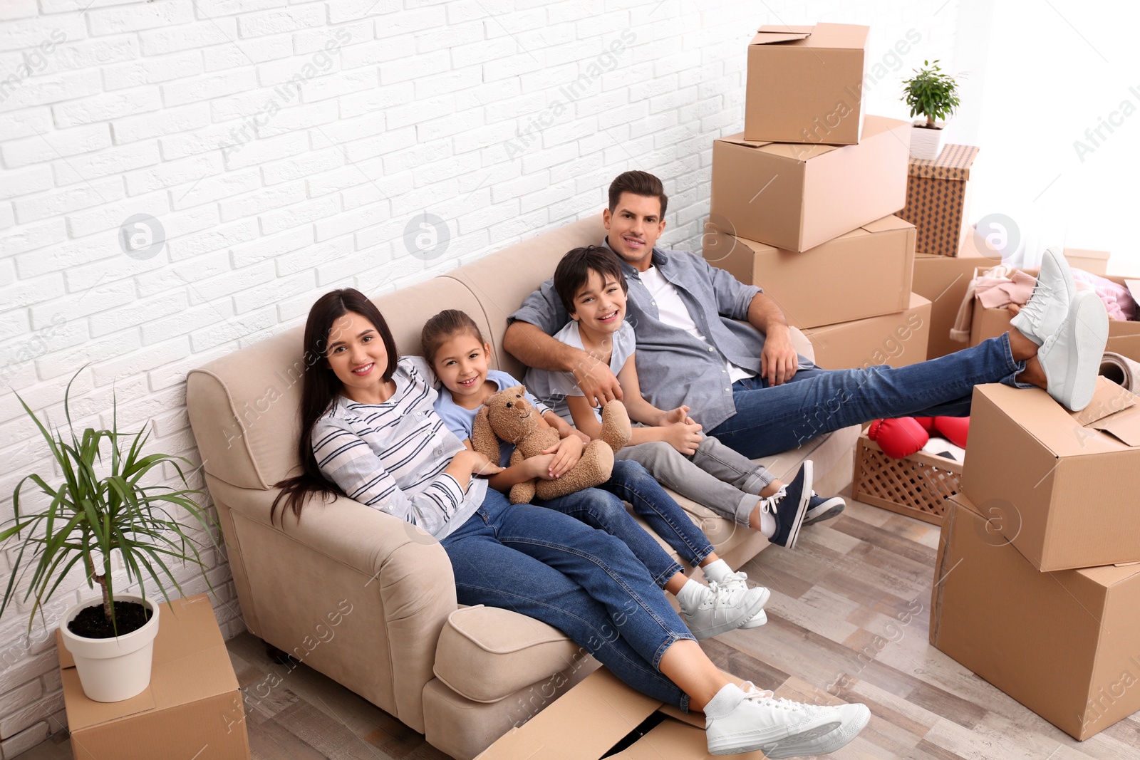 Photo of Happy family resting in room with cardboard boxes on moving day