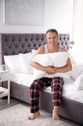 Photo of Happy man with soft pillow sitting on bed at home