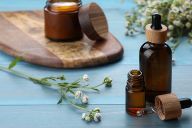 Bottles of essential oil with chamomile flowers on light blue wooden table, closeup. Space for text