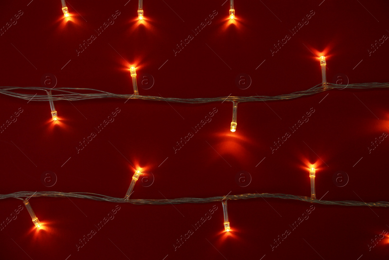 Photo of Glowing Christmas lights on red background, top view