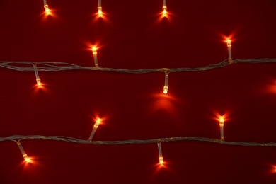 Photo of Glowing Christmas lights on red background, top view