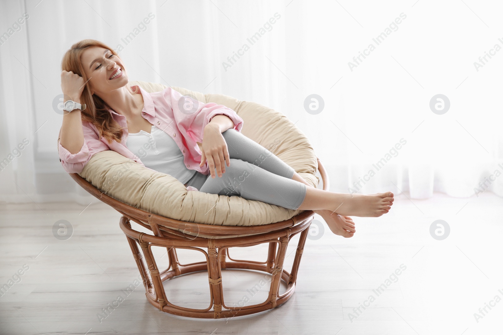 Photo of Young woman relaxing in papasan chair near window at home