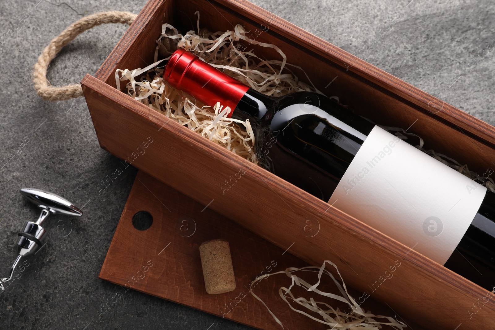 Photo of Bottle of wine in wooden box, cork and corkscrew on dark textured table, above view