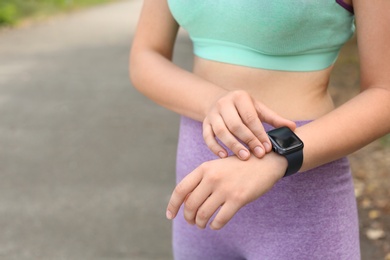 Young woman checking pulse with smartwatch after training on street, closeup. Space for text