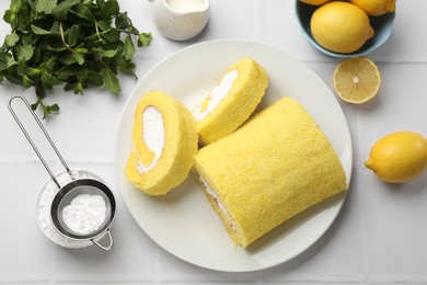 Photo of Delicious cake roll, lemons, mint and powdered sugar on white tiled table, flat lay